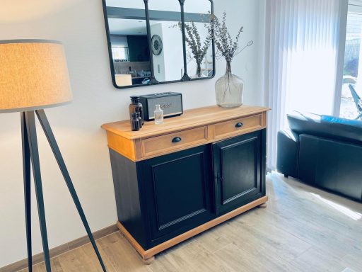 Meuble en bois bicolore avec miroir, lampe et vase sur une surface lumineuse.