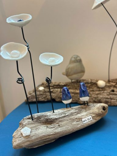 Composition artistique avec des fleurs en métal, une figurine et des éléments en bois.