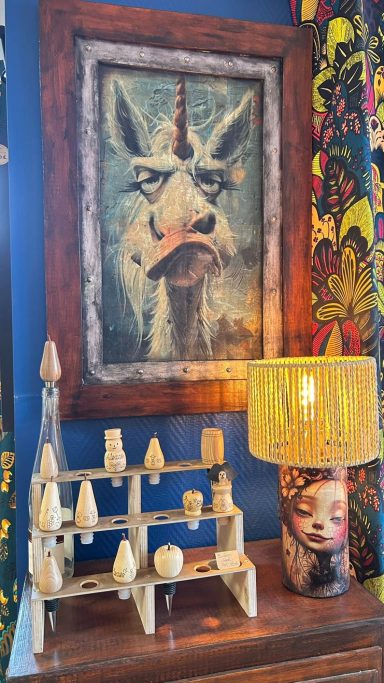 Table avec des objets décoratifs, un tableau d’un licorne et une lampe colorée.